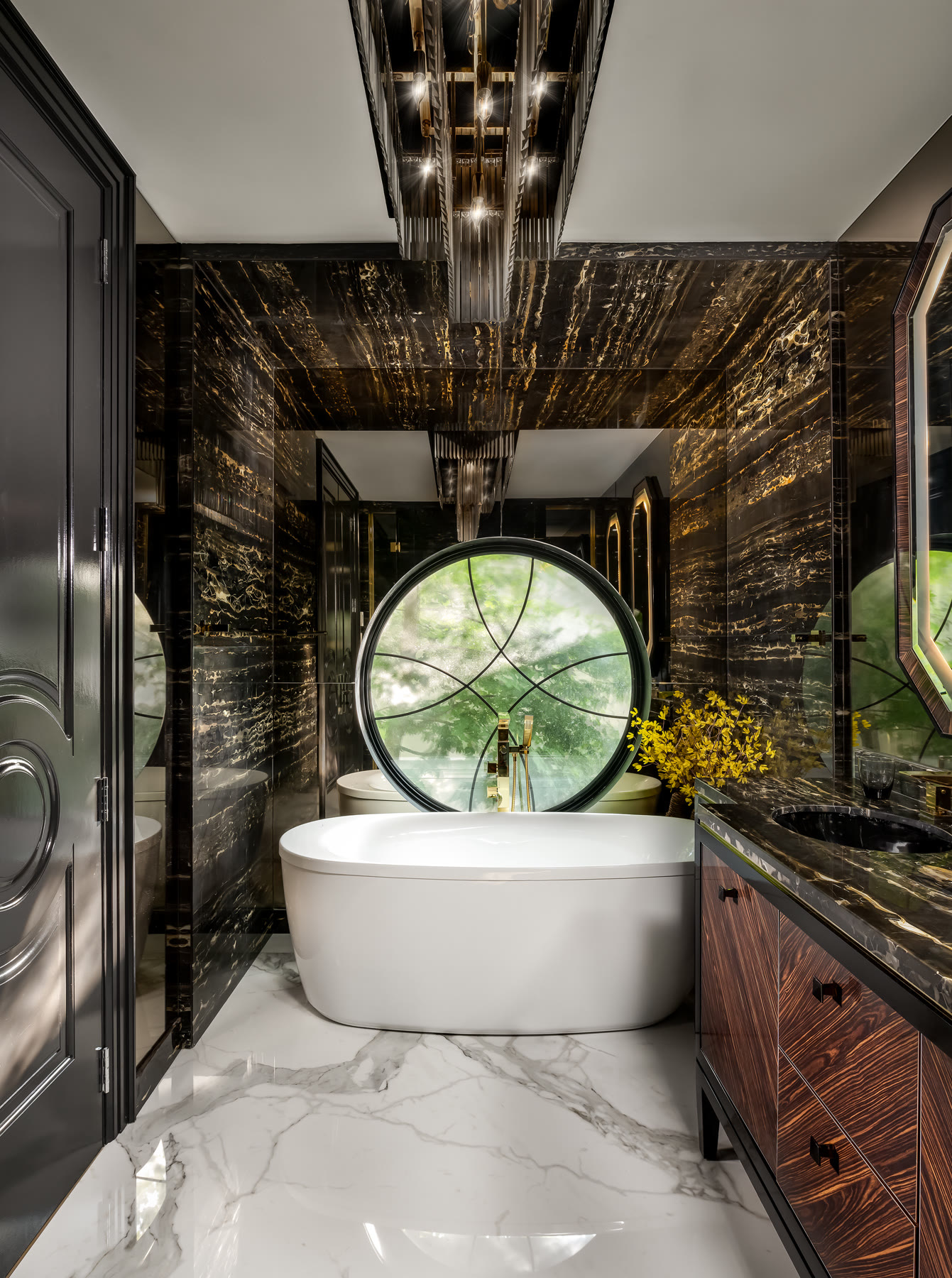 Freestanding tub in a black marble bathroom with a round window overlooking greenery